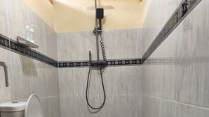A bathroom with a toilet, a shower, and tiled walls. - Sunflower Villa (Gili Trawangan)