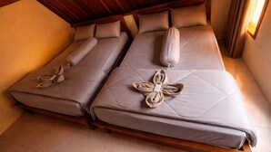 Two single beds with pillows and towels, wooden headboard, tiled floor, and a window with curtains. - Sunflower Villa (Gili Trawangan)
