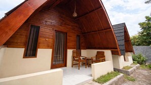 A wooden cabin with a pitched roof, a porch with two chairs, and a small window. - Sunflower Villa (Gili Trawangan)