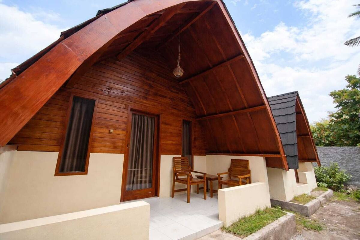 Una cabaña de madera con techo inclinado, un porche con dos sillas y una ventana pequeña.