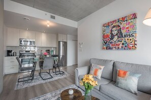 Eine moderne Küche mit Edelstahlgeräten, ein Essbereich mit Tisch und Stühlen sowie ein Wohnzimmer mit Sofa und Kissen.