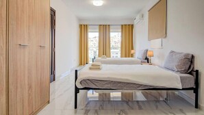 Habitación de hotel con cama, mesitas de noche, armario y vistas a edificios a través del ventanal.