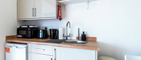 A compact kitchen with white cabinets, a microwave, a coffee maker, and a sink.