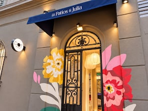 Entrada de un edificio con toldo azul, un letrero circular y una puerta metálica decorativa.