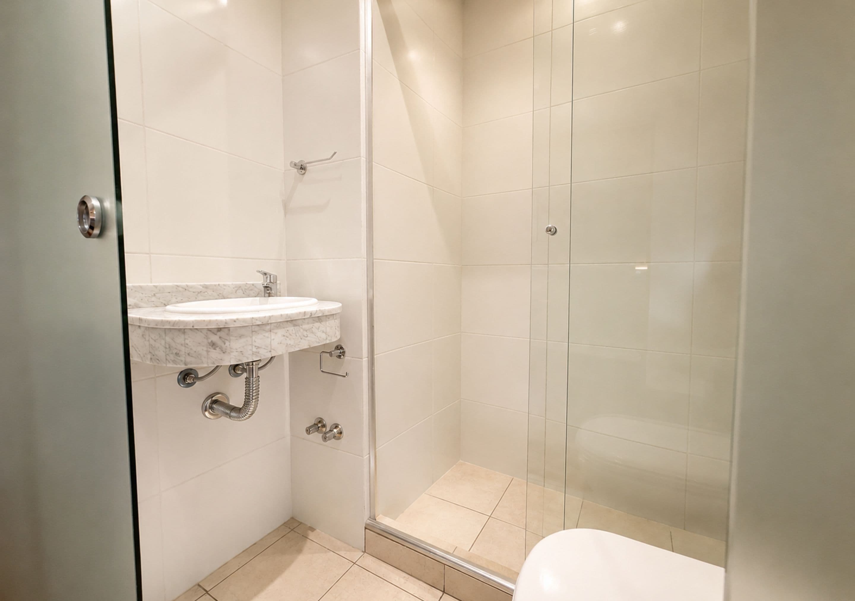 Un baño con cabina de ducha de vidrio, lavamanos de mármol y un inodoro.