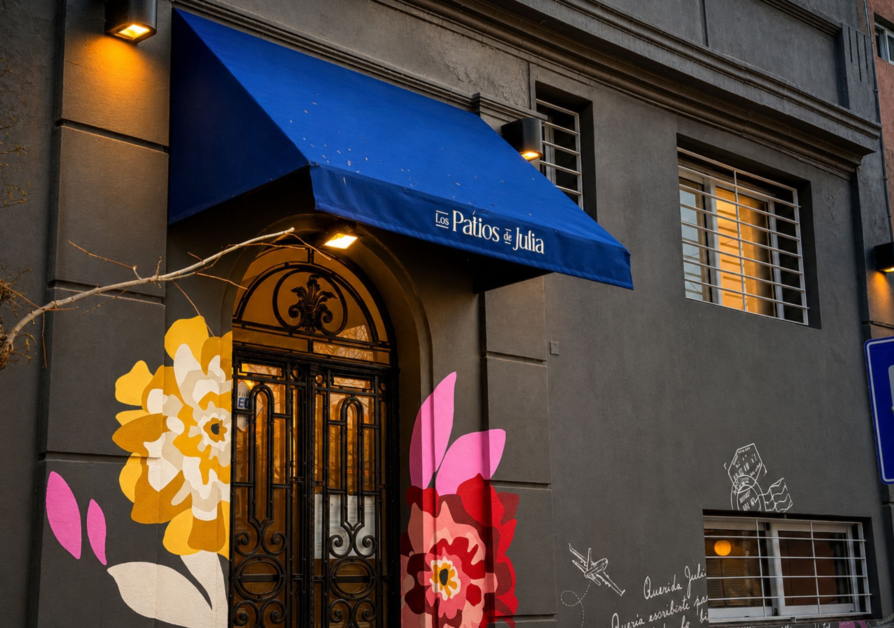 A building facade with a blue awning, large floral decorations, and a sign reading 'Los Patios de Julia'.
