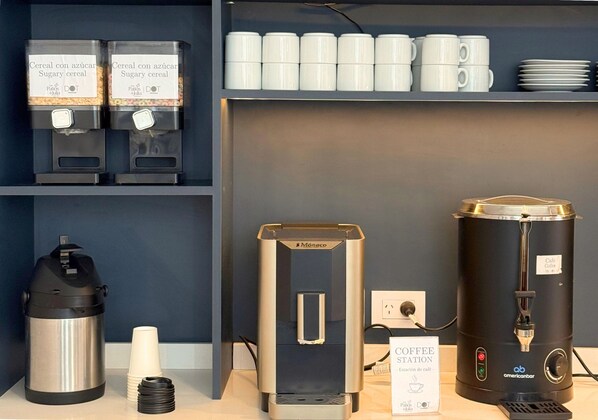 Una estación de café con cafetera, espumador de leche y una jarra de café.