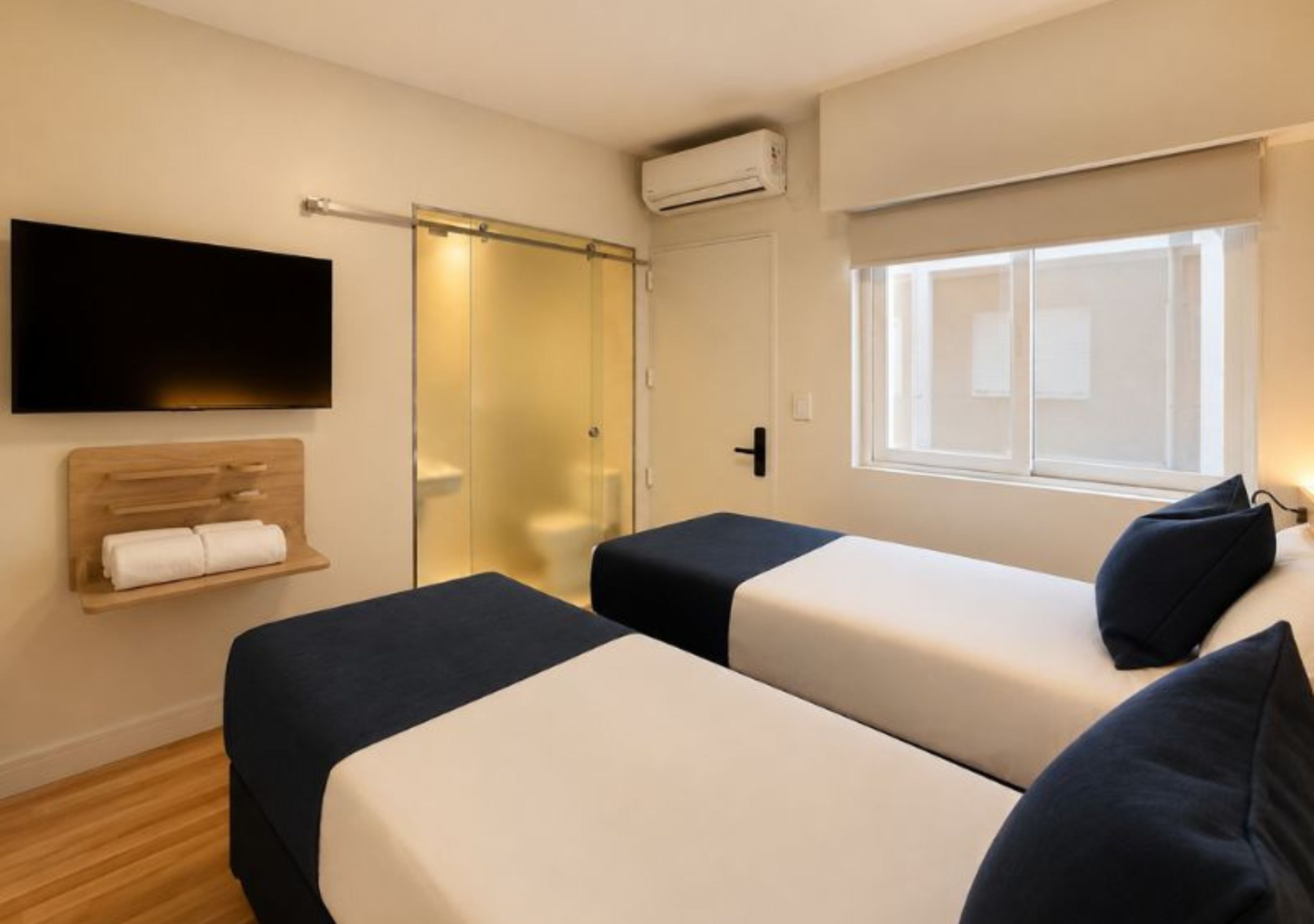A hotel room with two beds, a TV, a sliding door, and a window.