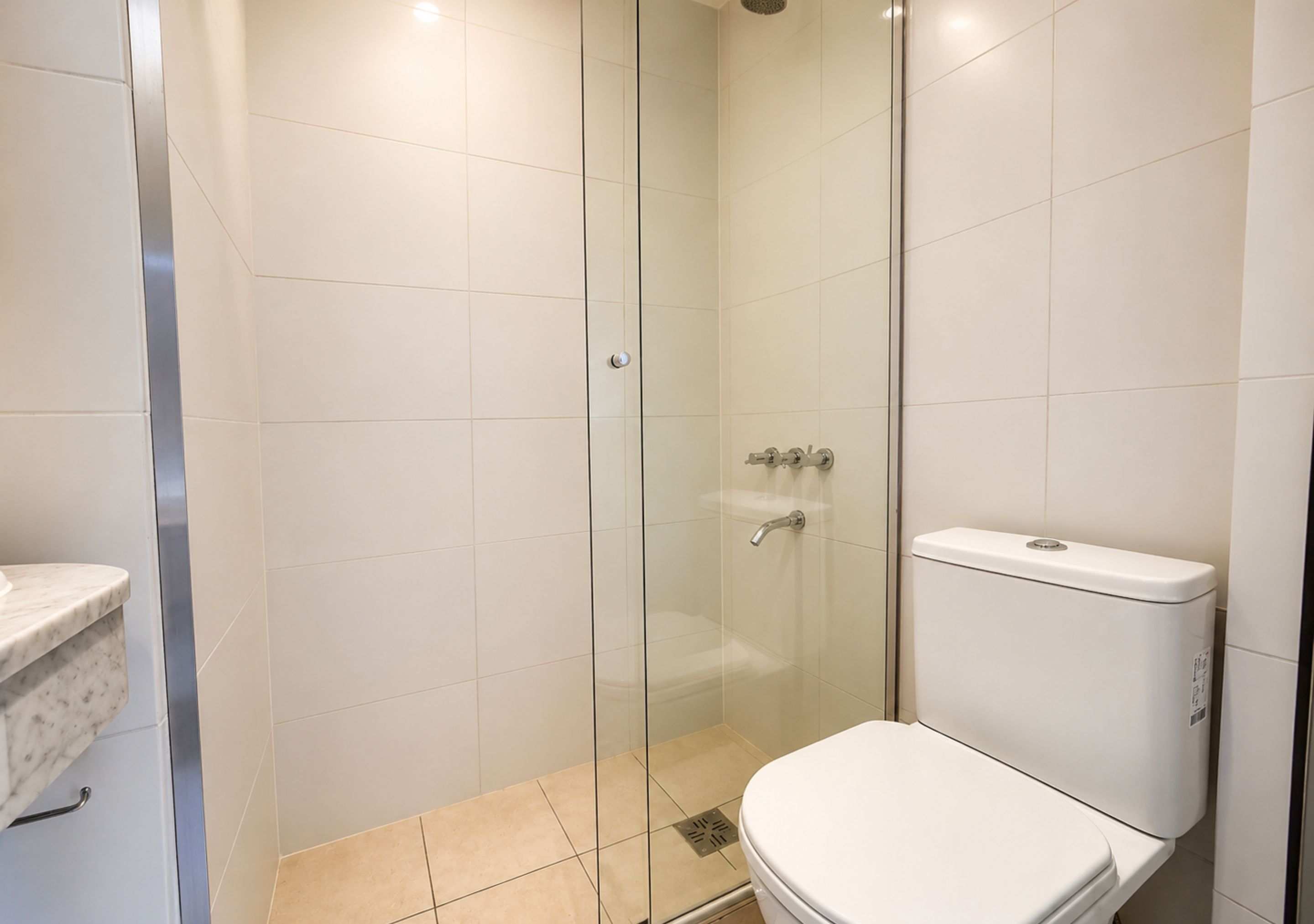 Un baño con ducha de vidrio, inodoro y lavamanos de mármol.