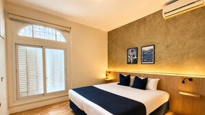 A bedroom with a large bed, wooden flooring, a window with shutters, wall-mounted air conditioning, and two framed pictures. - Los Patios de Julia by DOT Boutique (Buenos Aires)