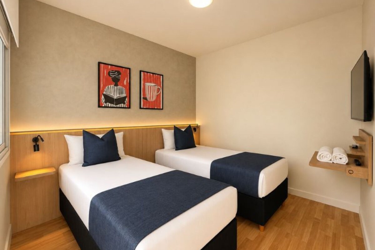 Habitación de hotel con dos camas, un estante con toallas y dos obras de arte en las paredes.