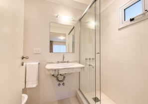 A modern bathroom with a glass shower enclosure, a marble sink, and a visible toilet.