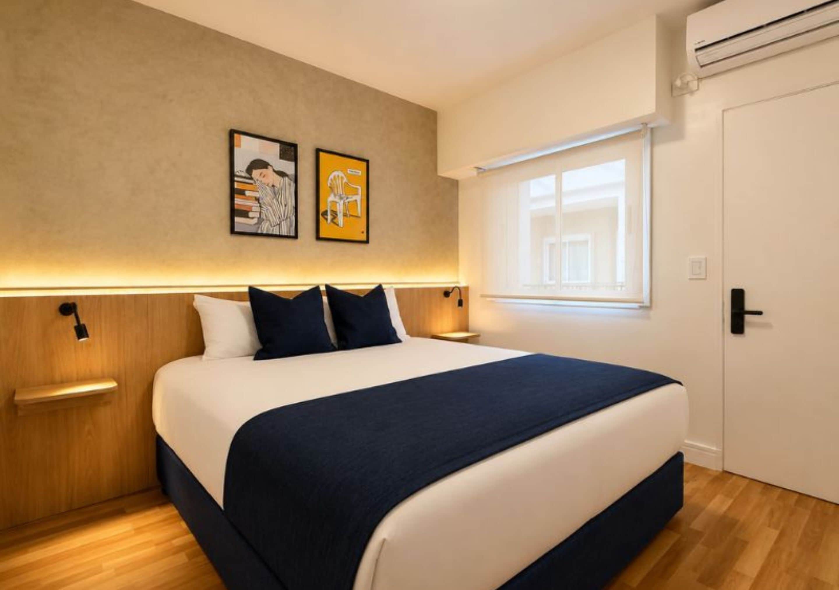 Une chambre à coucher avec un lit, des tables de chevet, une fenêtre et des œuvres d’art murales.