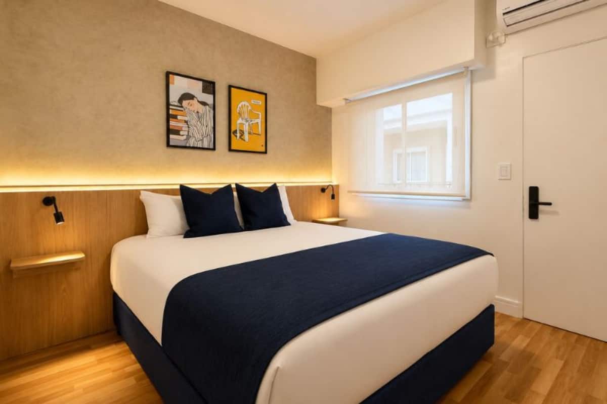 A bedroom with a bed, bedside tables, a window, and wall art.