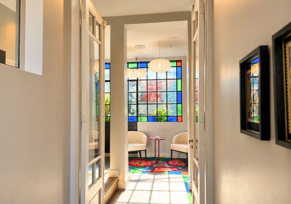 A hallway with a colorful stained glass window, white walls, and a small table with chairs.