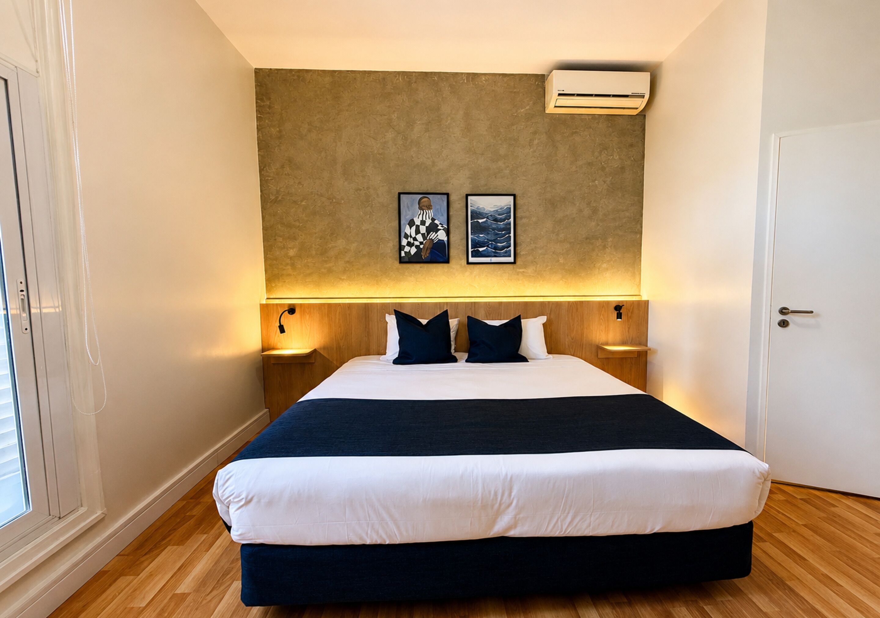Habitación de hotel con una cama grande, dos aires acondicionados instalados en la pared y dos cuadros enmarcados.
