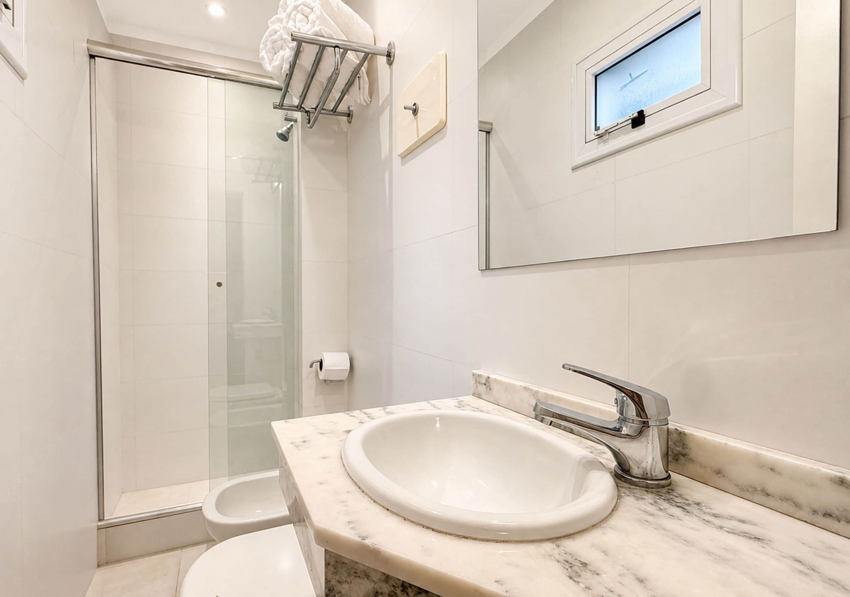 Un baño moderno con ducha envuelta en cristal, lavamanos de mármol y un ventanal con vistas.