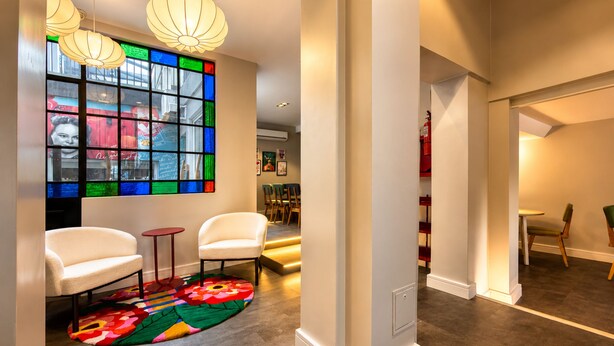 A modern interior with a large stained glass window, white chairs, a colorful rug, and pendant lighting. - Los Patios de Julia by DOT Boutique (Buenos Aires)