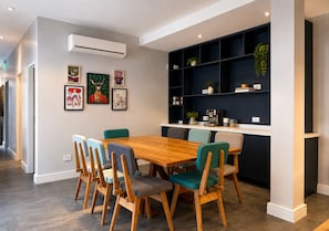 Un coin repas avec une table et des chaises en bois, une étagère sombre agrémentée de plantes et des œuvres d’art encadrées accrochées au mur.