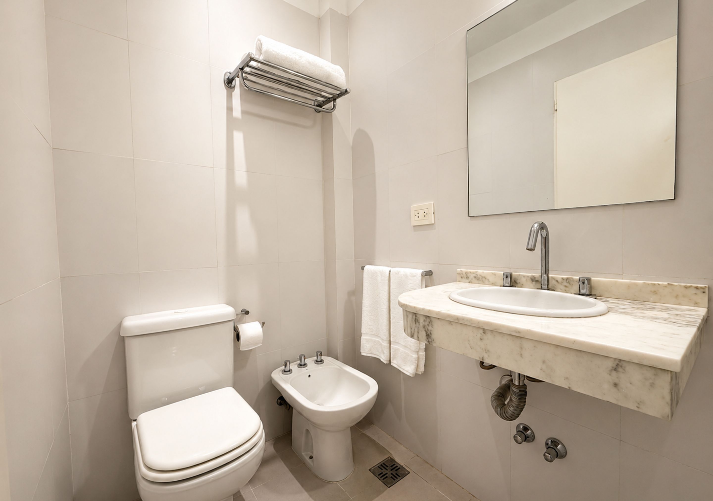 A bathroom with a toilet, bidet, sink, and mirror.