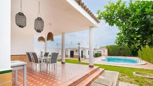 Eine überdachte Terrasse mit Gartenmöbeln, einem Swimmingpool und einem Garten.