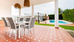 Eine Terrasse im Freien mit Esstisch und Stühlen, einem Pool und einem gepflegten Heckenstreifen.