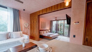 A modern hotel room with a sofa, a dining table with a bowl and spoon, a bed, and a TV mounted on the wall. - Modern 3BR Villa with 2 Pools & Rooftop Lounge (Tulum)