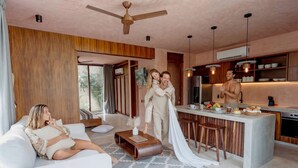 A modern living room with a sofa, a coffee table, a kitchen area with a bar, and a ceiling fan. - Modern 3BR Villa with 2 Pools & Rooftop Lounge (Tulum)