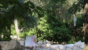 Un muro de piedra, un caballete de madera con una pintura, y abundante follaje en un jardín.