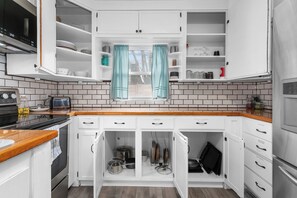 Een keuken met witte kastjes, een raam met gordijnen, een magnetron en een fornuis.