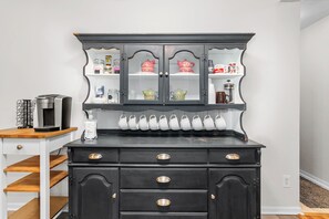 Een zwarte dressoir met glazen kastjes, een koffiezetapparaat en een fles handzeep.