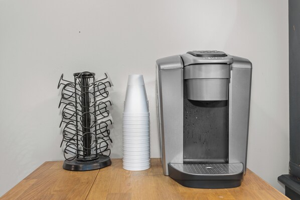 Une machine à café et un présentoir en métal avec des tasses, le tout posé sur une table en bois devant un mur uni.