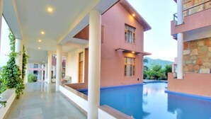 A modern hotel with a swimming pool, large windows, and a covered walkway. - OPO Palm Villa Dritan (Udaipur)