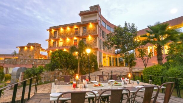 An outdoor dining area with tables and chairs, a stone building with warm lighting, and a staircase leading to the upper levels. - OPO Palm Villa Dritan (Udaipur)