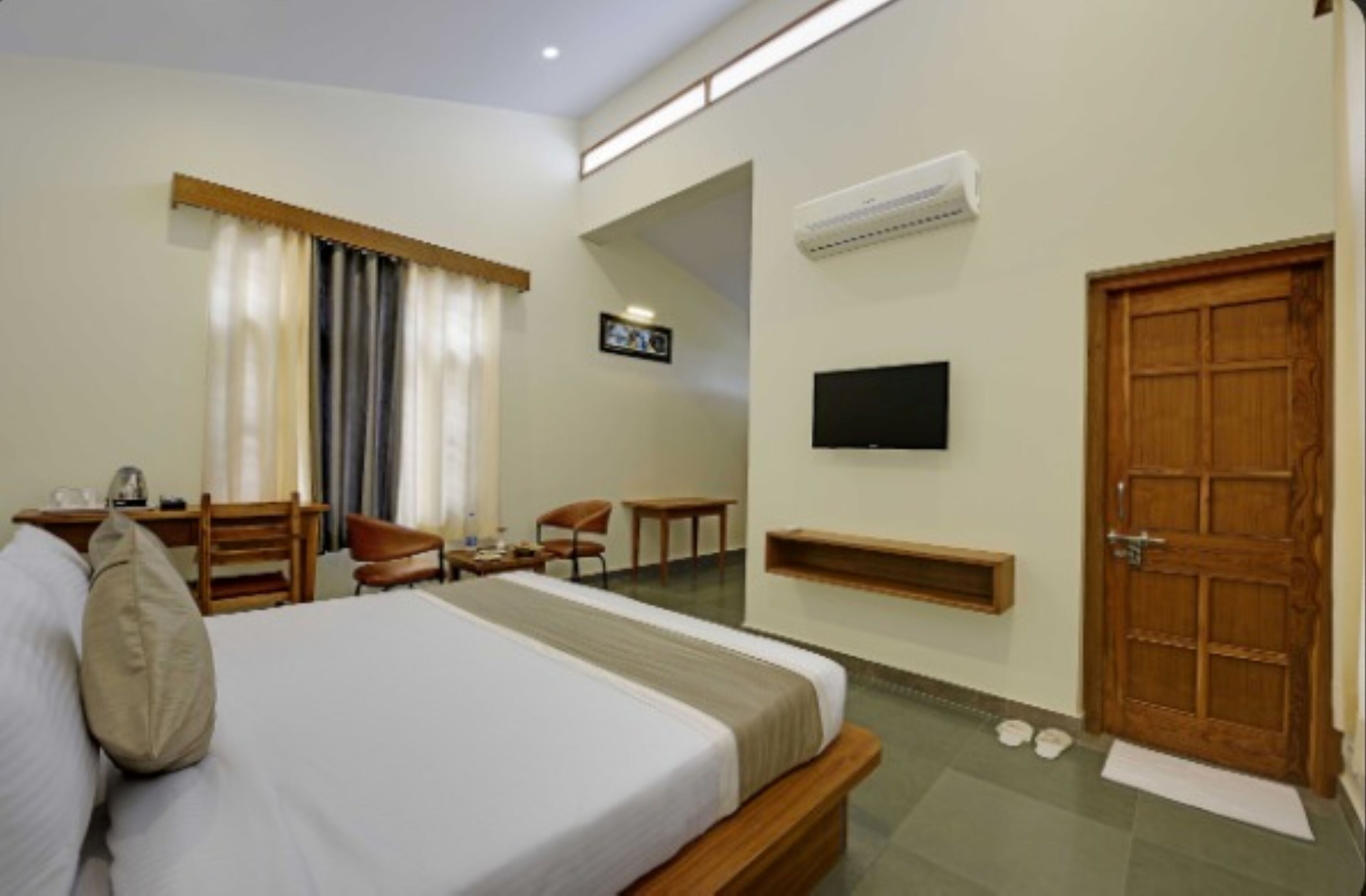 A hotel room with a bed, a desk, a chair, a TV, and a wooden door.