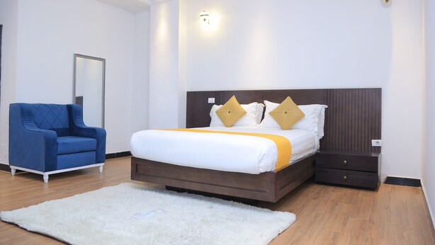 A bedroom with a bed, a blue armchair, a white rug, and a nightstand. - yellow apple hotel (Addis Ababa)