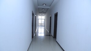 A corridor with doors on both sides, a tiled floor, and a view of a balcony with railings. - yellow apple hotel (Addis Ababa)