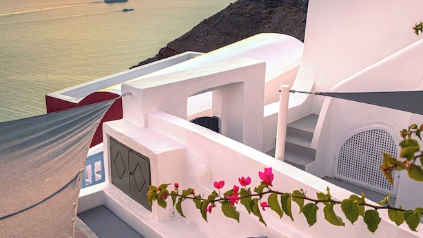 Un edificio blanco con piscina, una hamaca y vista al mar al atardecer.