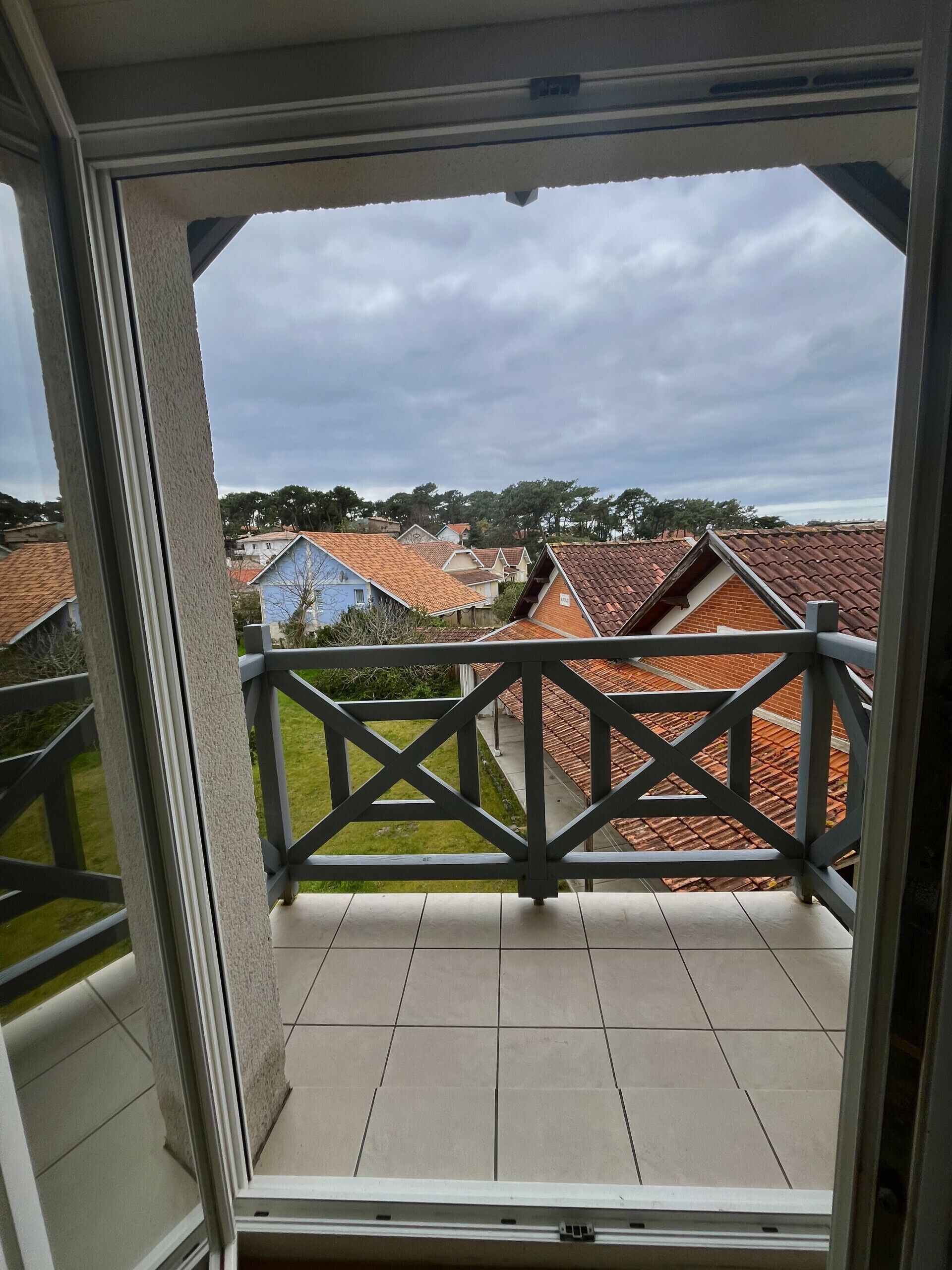 A balcony with a view of neighboring houses and a cloudy sky.