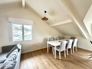 Ein Essbereich mit einem weißen Tisch und grauen Stühlen, ein Fenster mit Blick auf Häuser und eine schräge Decke.