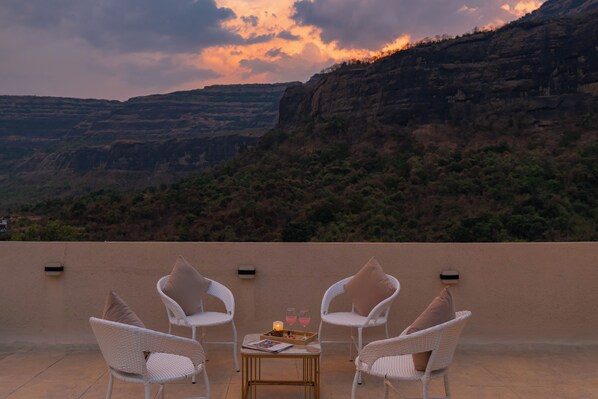 A terrace with white wicker chairs, a small table, and a tray with glasses and candles. - Heavenly Homes by ELIVAAS 2BHK Villa  (Karjat)