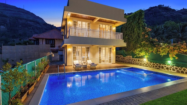 Una casa de dos pisos con piscina, mobiliario exterior y vistas a las montañas.