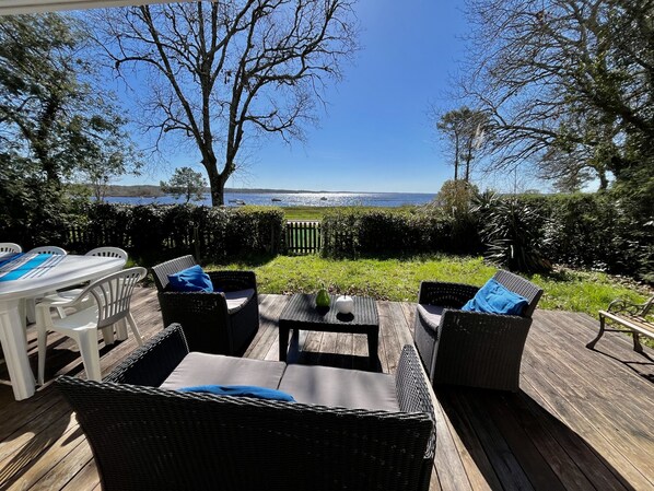 An outdoor patio with wicker furniture, a table, and chairs, overlooking a body of water.