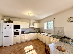 A kitchen with white cabinets, a refrigerator, a stove, a window, and a clock on the wall.