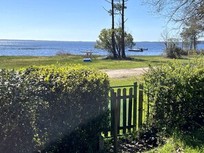 A grassy area with a wooden gate, a picnic table, and a boat docked by the water.
