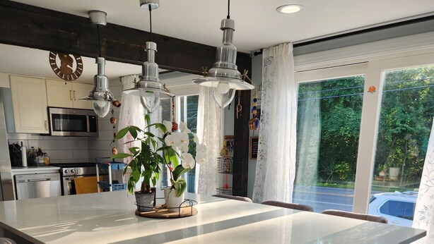 A modern kitchen with a large island, bar stools, pendant lighting, and a view of the outdoors.