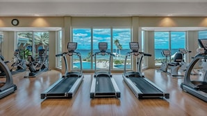 A gym with treadmills and exercise bikes, large windows with a view of the ocean, and a clock on the wall. - Luxury Portofino Condo | Panoramic Water Views | Pools, Spa & Beach (Pensacola Beach)
