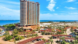 A high-rise hotel with a beach view, multiple balconies, and a parking area with covered parking structures. - Luxury Portofino Condo | Panoramic Water Views | Pools, Spa & Beach (Pensacola Beach)