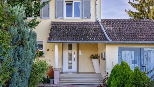 Una casa con techo de tejas, una puerta principal y escalones que llevan a la entrada.
