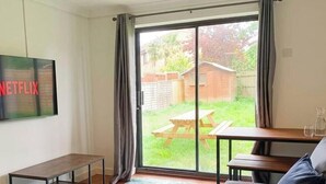 En stue med et fjernsyn der viser Netflix-logoet, en skydedør til en baghave, et træbord og en sofa.